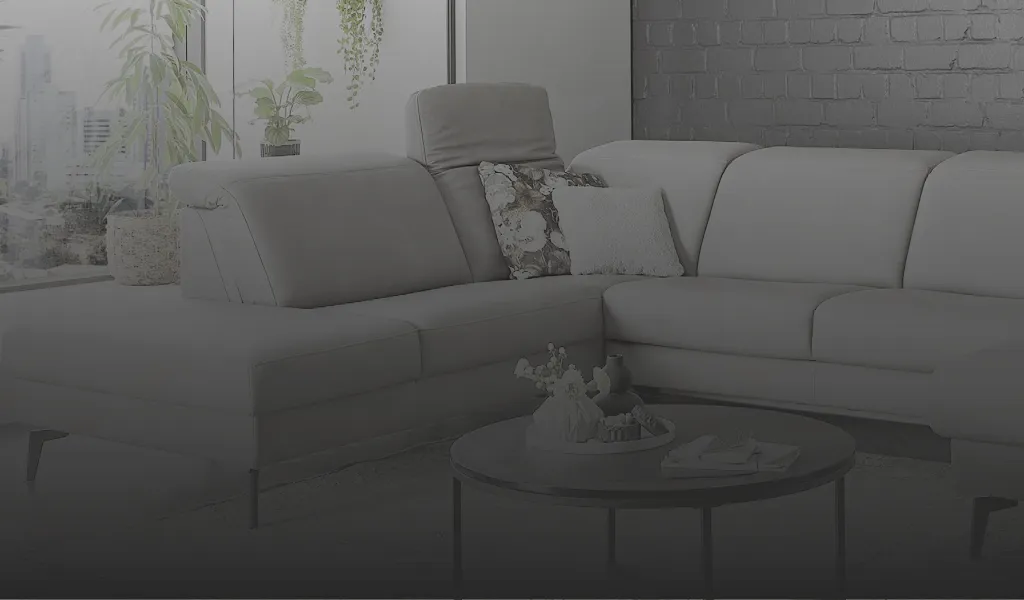 Stilvolles hellgraues Ecksofa mit verstellbaren Kopfstützen, gemütlichen Dekokissen und schwarzem Couchtisch im modernen Wohnzimmer mit Backsteinwand und Pflanzen. Perfekt für Wohnen mit Komfort und Design.